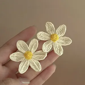 Close-up of summer style woven daisy earrings with white petals and yellow center
