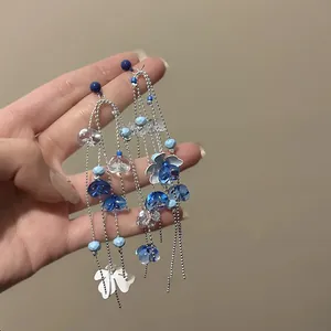 Close-up of long blue floral tassel earrings with delicate silver chains and beads