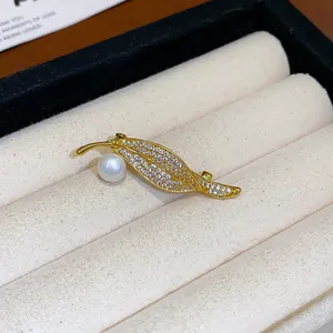 Détail de l'élégante broche feuille plaquée or avec des zircons et une perle blanche.