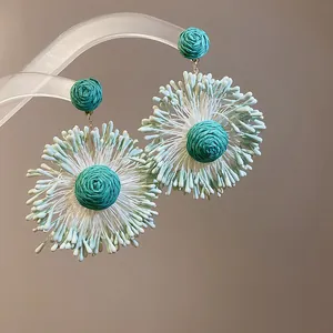 Close-up of handmade teal floral cluster drop earrings with woven texture