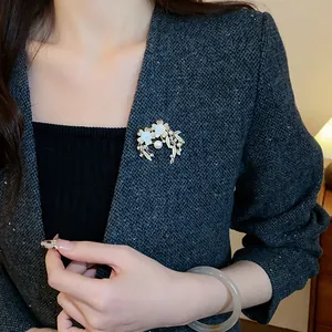 Élégante broche florale dorée avec zircon et perle sur un blazer en tweed gris foncé.