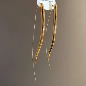 Macro view of long polished gold curved drop earrings with smooth metallic finish