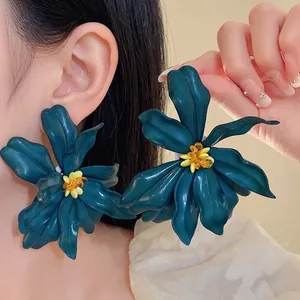 Oversized teal acrylic flower stud earrings with yellow beaded centers on Asian model.