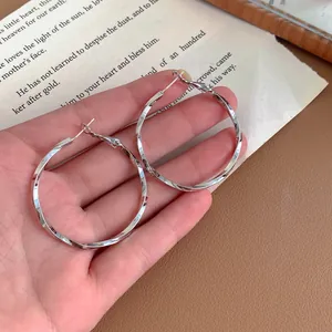 Close-up detail of stylish silver-toned twisted hoop earrings being held for size reference