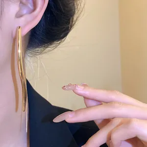 Close-up of elegant gold glossy teardrop long ear hook earrings worn for a stylish look