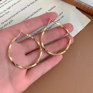 Close-up view of large golden twisted hoop earrings with minimalist spiral design.