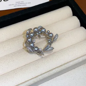 Gros plan d'une élégante broche couronne avec perles grises et zircons dans un écrin