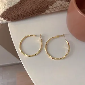 Close-up of elegant gold twisted hoop earrings displayed on a minimalist background