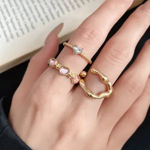 Detail view of three elegant gold rings with pink heart stones and molten texture on finger