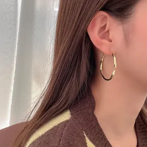 Detailed view of a golden twisted C-shaped hoop earring on a model's ear