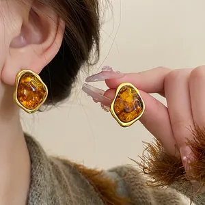 Retro Maillard style amber resin earrings with gold edges shown on ear and hand