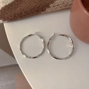 Close-up of minimalist twisted silver hoop earrings with a sleek metallic finish.