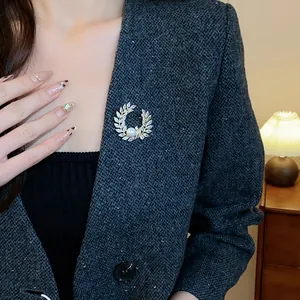Gros plan d'une élégante broche couronne de laurier avec zircone et perle sur tweed gris
