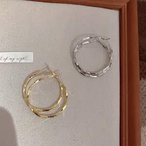 Close-up detail of gold and silver twisted hoop earrings on a light fabric display board