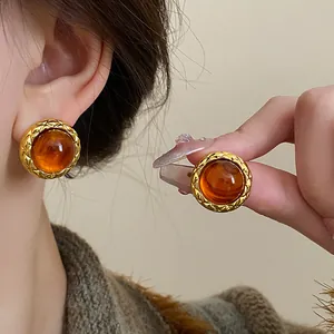 Macro detail of vintage-style gold quilted stud earrings featuring an amber-colored resin cabochon