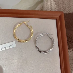 Close-up shot of gold and silver twisted hoop earrings presented on a neutral display tray