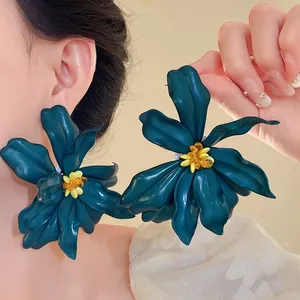 Close-up of oversized dark teal acrylic flower earrings with yellow bead centers.
