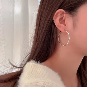 Close-up of a silver twisted hoop earring worn by a model in a minimalist style.