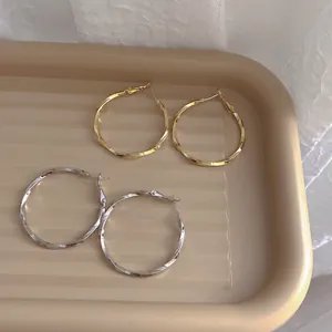 Minimalist twisted hoop earrings in gold and silver finishes on a stylish tan tray