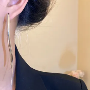 Detail view of a long, sleek silver water-drop ear hook earring on a model
