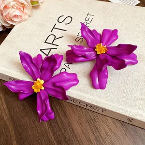 Detailed view of oversized purple acrylic flower stud earrings on a textured book background.