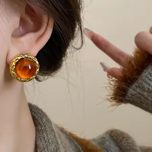 Close-up of a model wearing retro amber-colored round stud earrings with gold trim