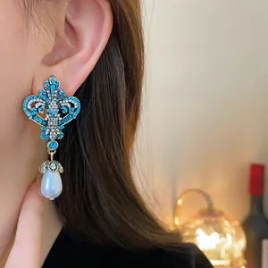 Close-up of vintage fleur-de-lis earrings with turquoise rhinestones and teardrop pearls.