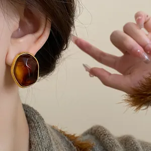 Close-up of a vintage brown oval earring with a gold twisted border worn on the ear.