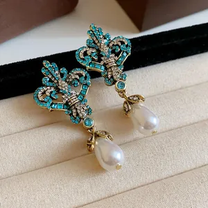 Detail view of vintage style gold earrings with blue crystals and elegant teardrop pearls.
