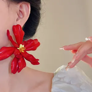 Detail view of large red acrylic flower earrings with yellow seed beads on model