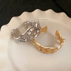 Irregular crumpled metal open bangles in gold and silver set on white scalloped plate