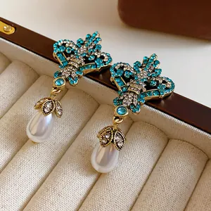 Close-up of vintage rhinestone and teardrop pearl earrings in a beige velvet jewelry box.