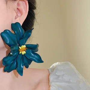 Close-up of an oversized teal blue acrylic flower earring with yellow beaded center details