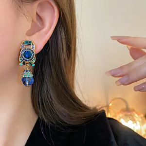 Macro detail of vintage geometric gold earrings with vibrant blue crystals worn on model's ear