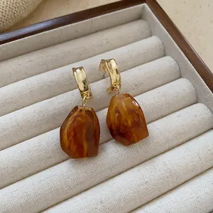Detailed view of vintage amber resin drop earrings with gold metal hoops in a tray