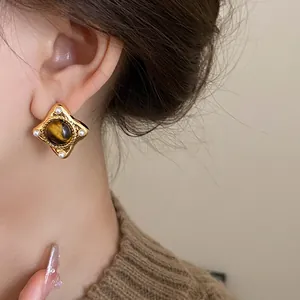 Close-up of retro geometric gold earring with brown stone on model's ear