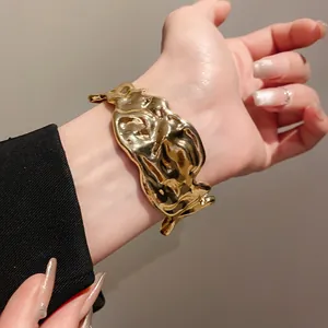 Detailed view of a gold-colored irregular wrinkled metal cuff bracelet worn on a wrist.