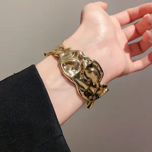 Detailed macro close-up view of irregular crumpled gold metal cuff bracelet on wrist
