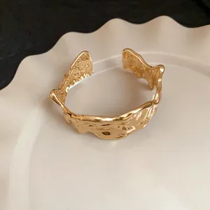 Macro view of gold irregular crumpled metal cuff bracelet on white plate