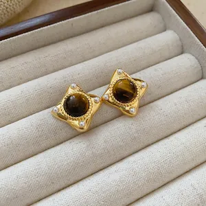 Close-up of vintage geometric gold stud earrings with brown tiger eye stone and pearls.