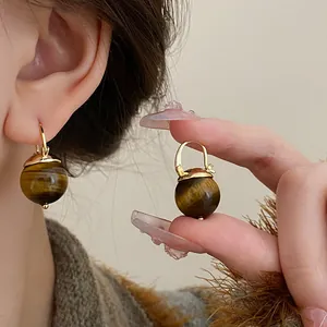 Detail view of retro tiger's eye ball earrings with gold-toned hooks on a model.