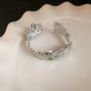 Detail view of irregular silver crumpled metal cuff bracelet on a white ceramic plate.