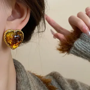 Close-up of amber heart-shaped stud earring on ear with gold textured bezel design