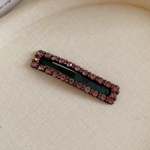 Detailed view of a black rectangular hair clip embellished with sparkling pink rhinestones.