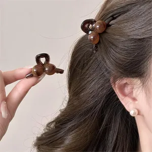 Detail of minimalist brown round mini hair claw clip worn on hair and held by hand