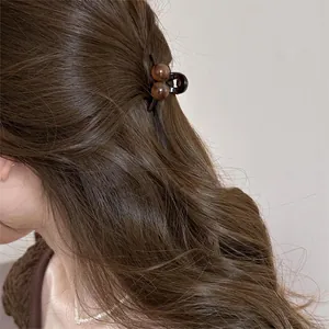 Close-up of a brown mini hair claw clip with round bead design on long wavy hair