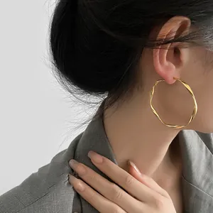 Detailed shot of elegant gold Mobius twisted large hoop earrings worn by a female model