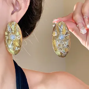 Primo piano di eleganti orecchini ovali dorati con trama a onde e perle centrali.