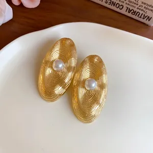 Dettaglio macro della trama a onde dorate su orecchini ovali con perla centrale.