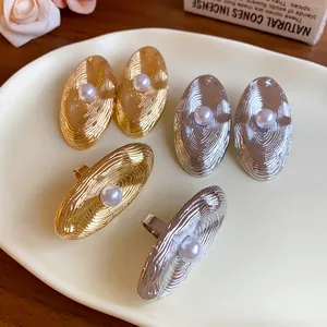 Dettaglio di orecchini ovali geometrici in oro e argento con perle centrali raffinate